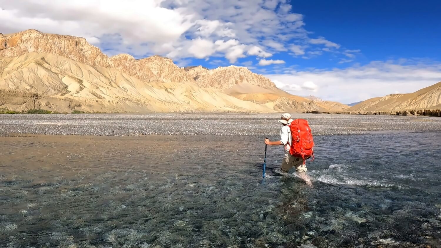 Wanderer mit Rucksack durchquert einen Bergfluss im Himalaya.