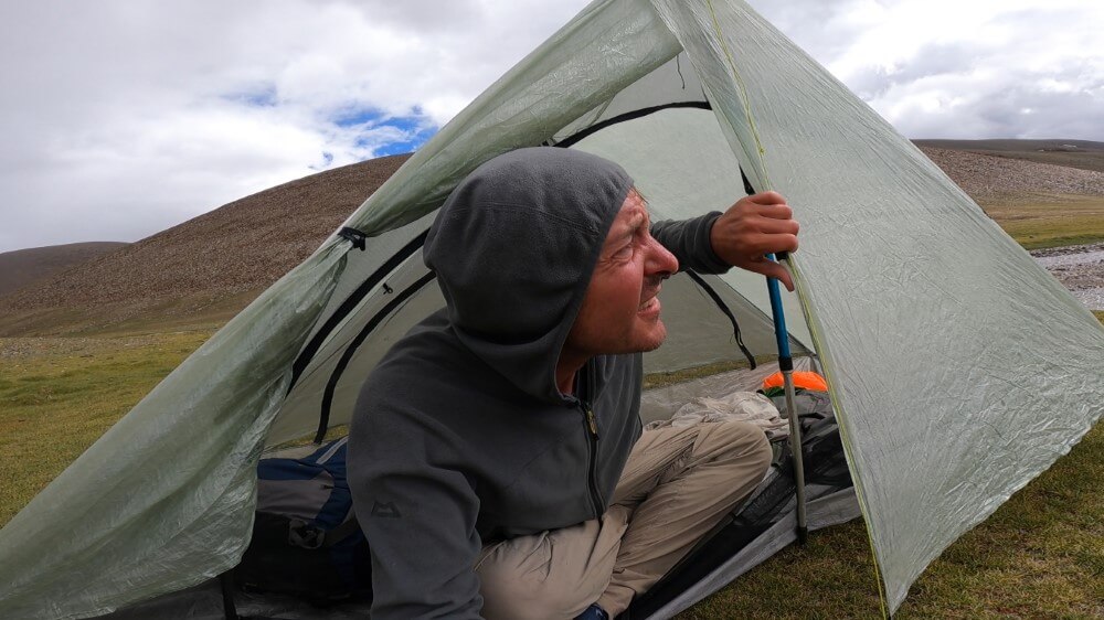 Trekker beim Zelten in Berglandschaft bei schlechtem Wetter.