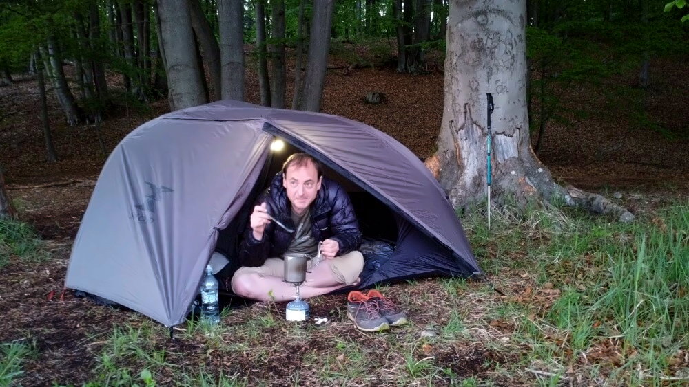 Wanderer im Wald sitzt im aufgebauten Decathlon MT900 1 Personenzelt.