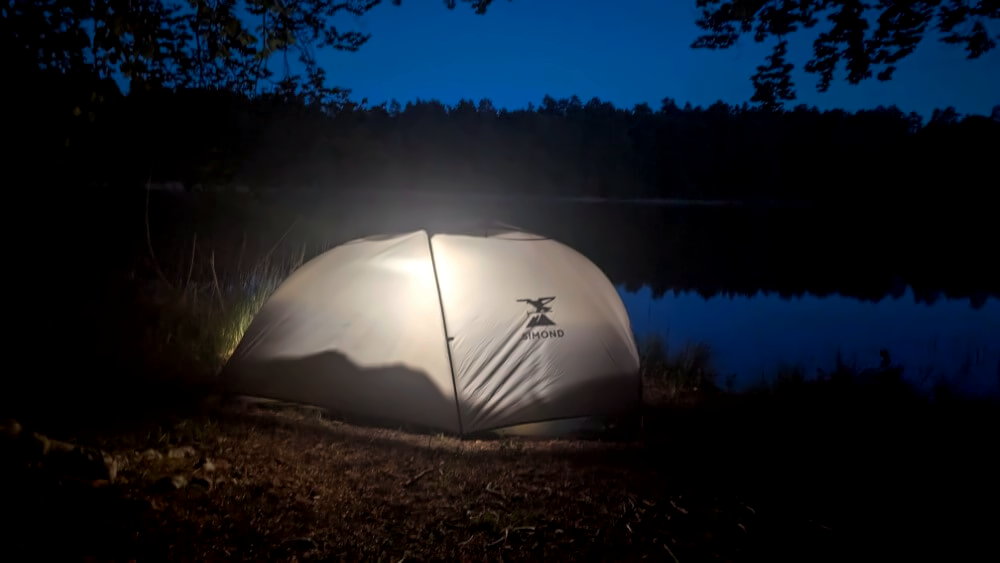 Decathlon MT900 1 Personenzelt bei Nacht am See mit angeschalteter Laterne.